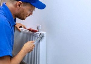 Loodgieter in blauw uniform repareert een radiator met een moersleutel.